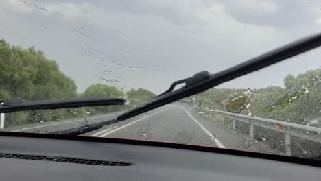 car driving on rural road in rainy weather , wipers removing water on front glass