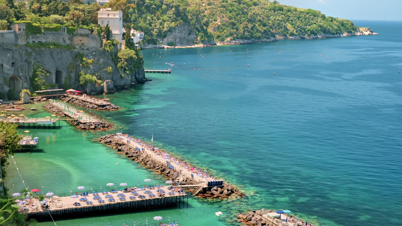 Vista della costa tirrenica a Sorrento, Italia. Pontili con lettini per il riposo, acqua trasparente, scogliere con edifici