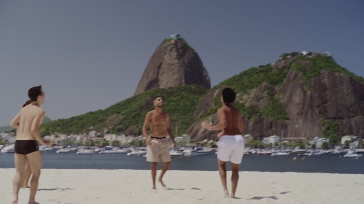A group of friends playing footvolley on a sunny beach in Rio de Janeiro with Sugarloaf Mountain in the background