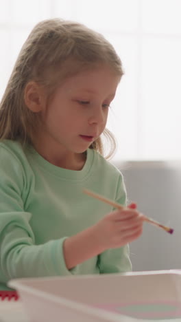 concentrated blonde girl drips paint into liquid doing ebru art with teacher in studio closeup slow motion. creative development for children