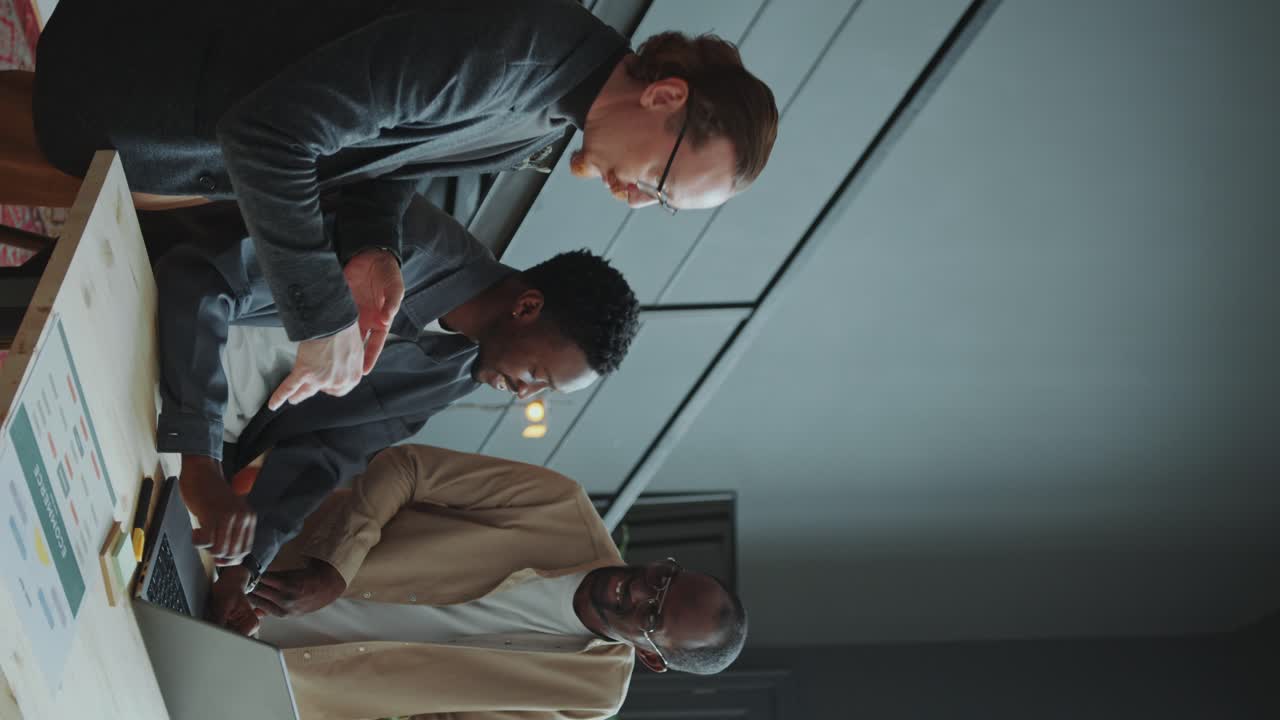Businessman Discussing Data On Laptop with Two Colleagues in Office