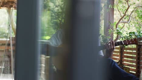 thoughtful african american senior man sitting on balcony playing acoustic guitar