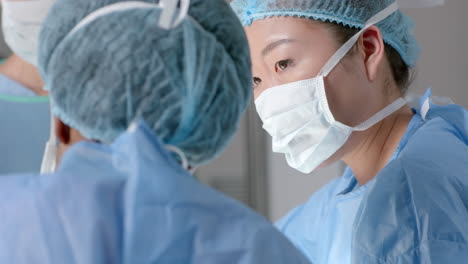 diverse female surgeons wearing surgical gowns discussing work in operating theatre, slow motion