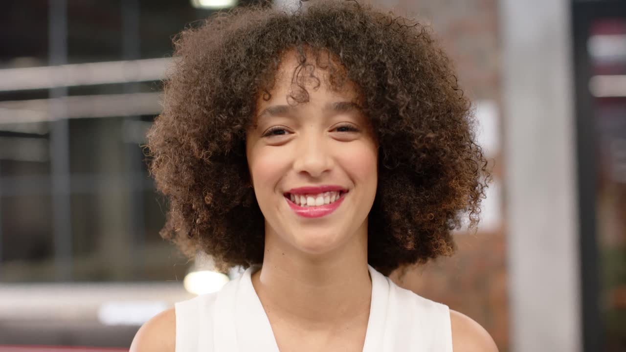 Portrait of happy biracial creative businesswoman smiling in office, in slow motion