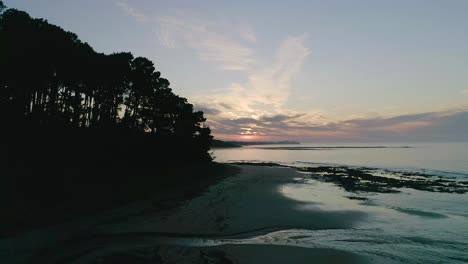 Drohnenaufnahme-Eines-Sonnenaufgangs,-Der-über-Einer-Strandlandschaft-Mit-Silhouettenkiefern-In-Shoreham-Aufsteigt