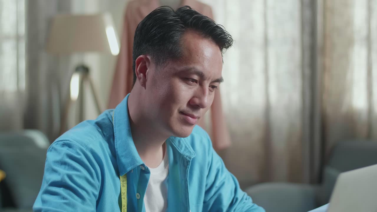 스튜디오에서 옷을 디자인하는 동안 노트북에서 일하는 아시아 남성 디자이너의 클로즈업