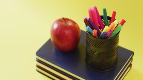 video of stack of books, markers in container and apple on yellow background