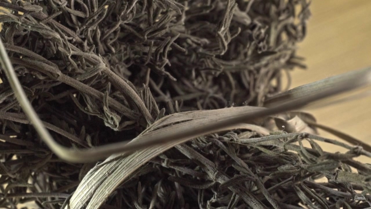 Macro close up showing dried rosemary herb with detailed leaf texture on wooden surface highlighting aromatic culinary spice used in cooking and food preparation