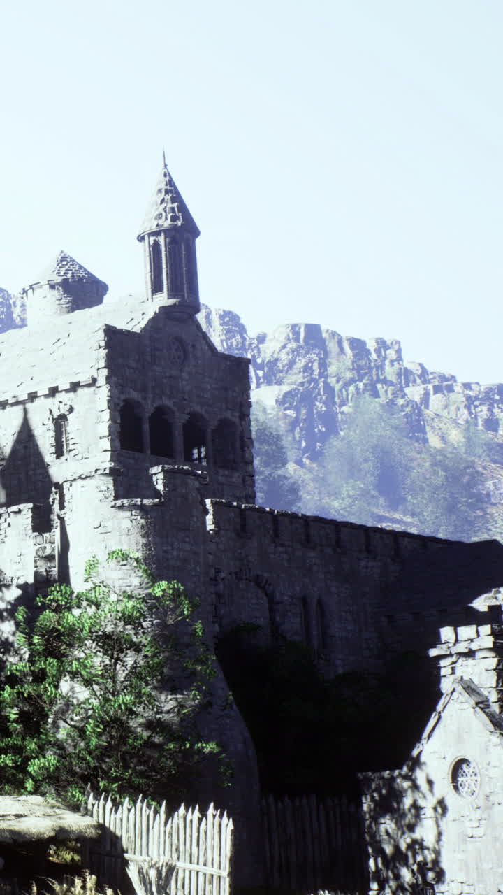 Ancient stone monastery stands against majestic mountain backdrop in sunlight