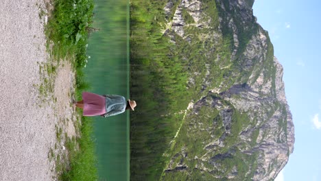 Woman-in-pink-skirt-surveys-shoreline-of-Lago-di-Landro-before-departing,-Dolomiti