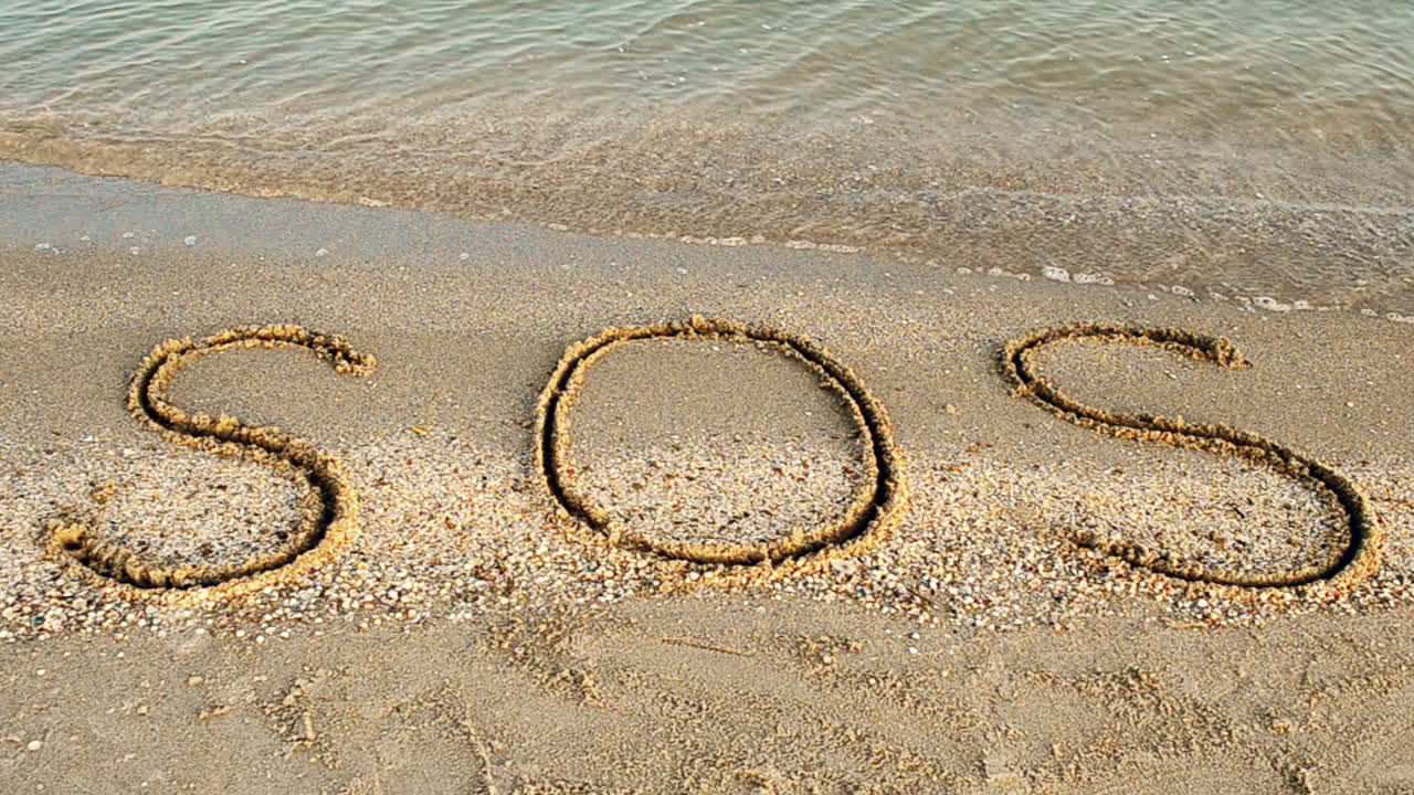 Inskriptionen SOS i sanden. Filmning på stranden