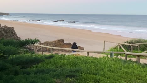 silhouette of a man sitting alone on the beach looks at the waves at the surf spot