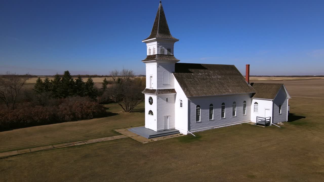 Low aerial orbit around St Boniface Catholic Church in Alberta, Canada. 4k footage of a white old abandoned country chapel made of wood in the early 20th century. Heritage buildings of Flagstaff