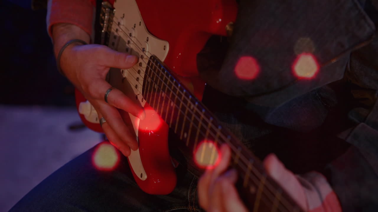 音楽スタジオで赤いエレキギターのフレットを押さえる男性ミュージシャン。アニメーションの音波ビジュアルが重ねられている。