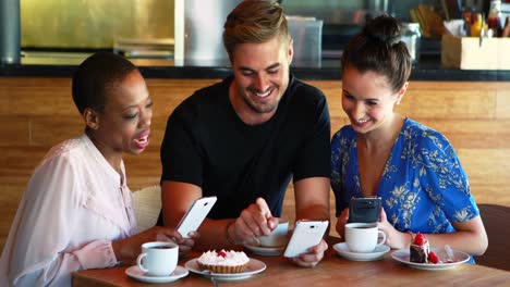 Amigos-Usando-El-Teléfono-Móvil-Mientras-Desayunan-Y-Toman-Café