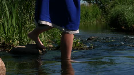 niña con vestido folk azul en la orilla del río lentamente puso la pierna en el río