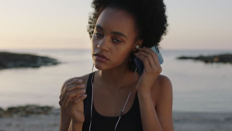 portrait of fit african american woman looking to camera puts on earphones listening to music using smartphone