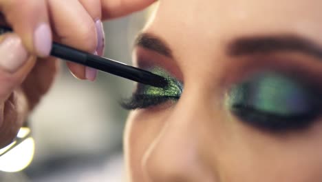 extremadamente cerca aplicando brillantes sombras verdes brillantes en la esquina de los ojos. hermoso modelo caucásico