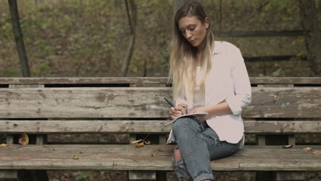 mujer joven se sienta en un parque forestal con un bloc de dibujo slider dolly shot