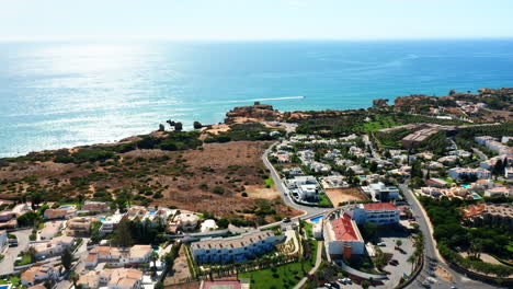 Aerial-orbiting-shot-of-beautiful-Algarve-Coastline-with-sunlight-reflection-in-ocean-water-and-hotel-resorts-with-pool-in-Portugal