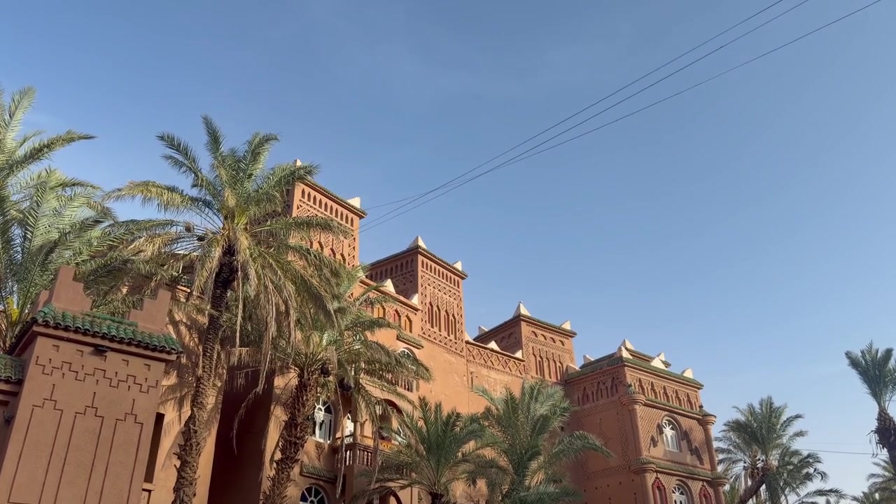 Edificio marocchino ornato con torri e palme sotto un cielo azzurro limpido, architettura del deserto.