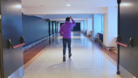 rear wide shot of man wearing purple hoodie and jeans, walking on hallway