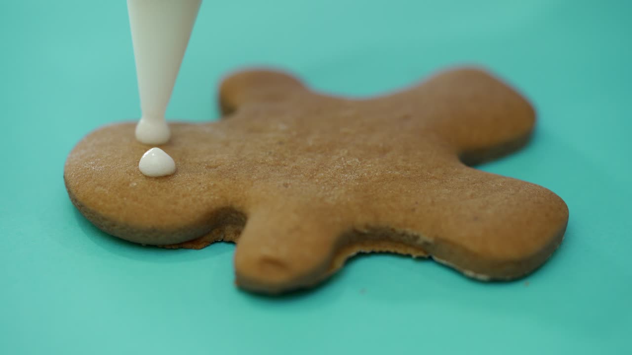 The confectionery nozzle is drawing the image of a person on the finished ginger biscuits with icing. Close-up. Christmas cookies