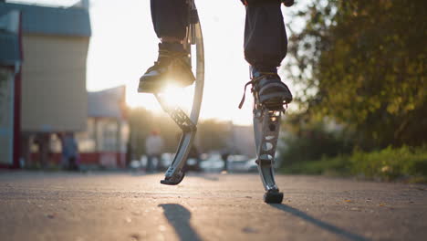 low-angle view of a person using spring stilts outdoors in an urban setting with trees, parked cars, and blurred background. the focus is on their legs and stilts, with light emphasizing the movement