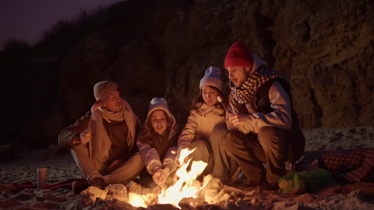 친구 들 이 밤 에 해변 에서 캠프 불 을 즐기고 있다