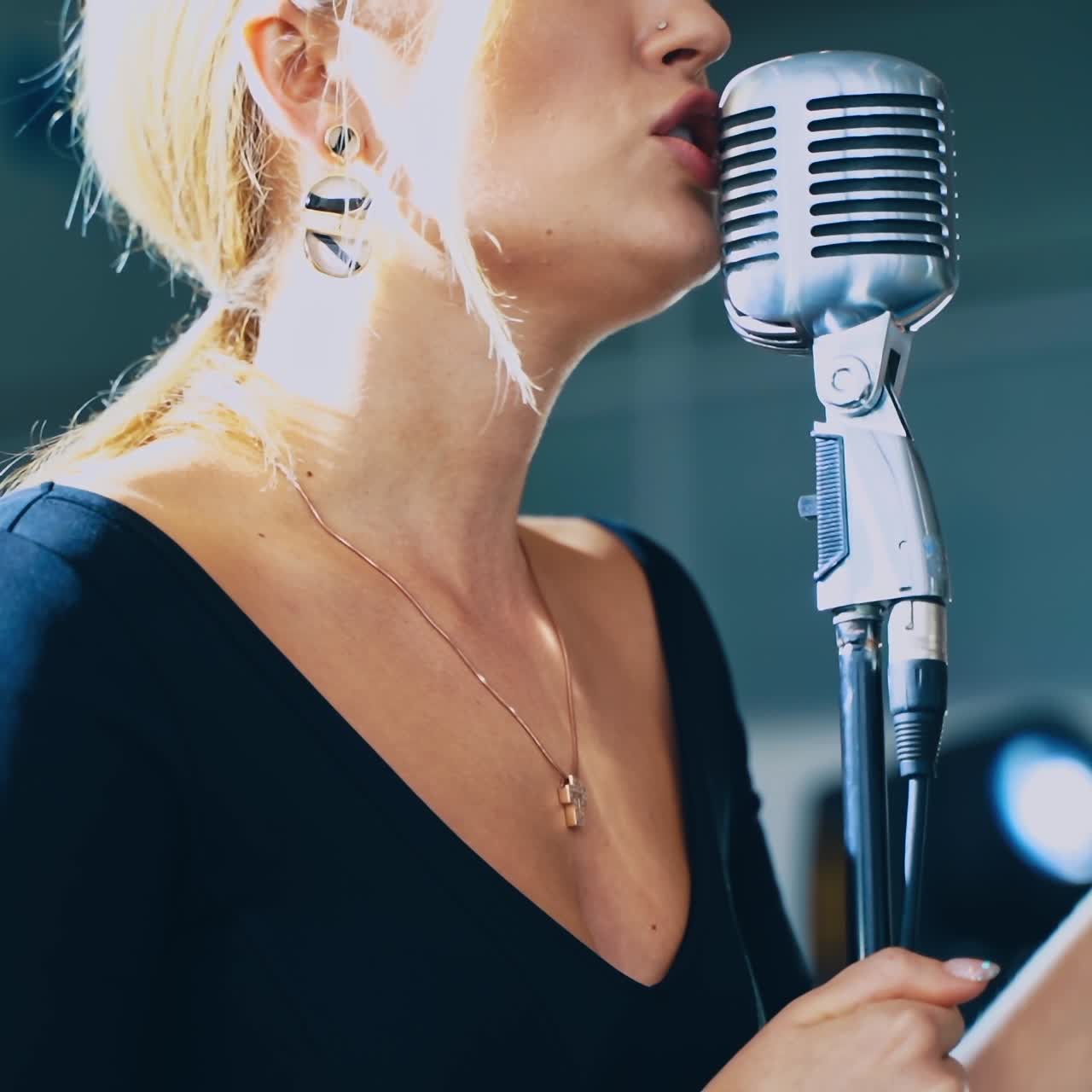 Side view of young professional female singer. Face of a beautiful girl performing song on stage into the microphone. Musical concert.