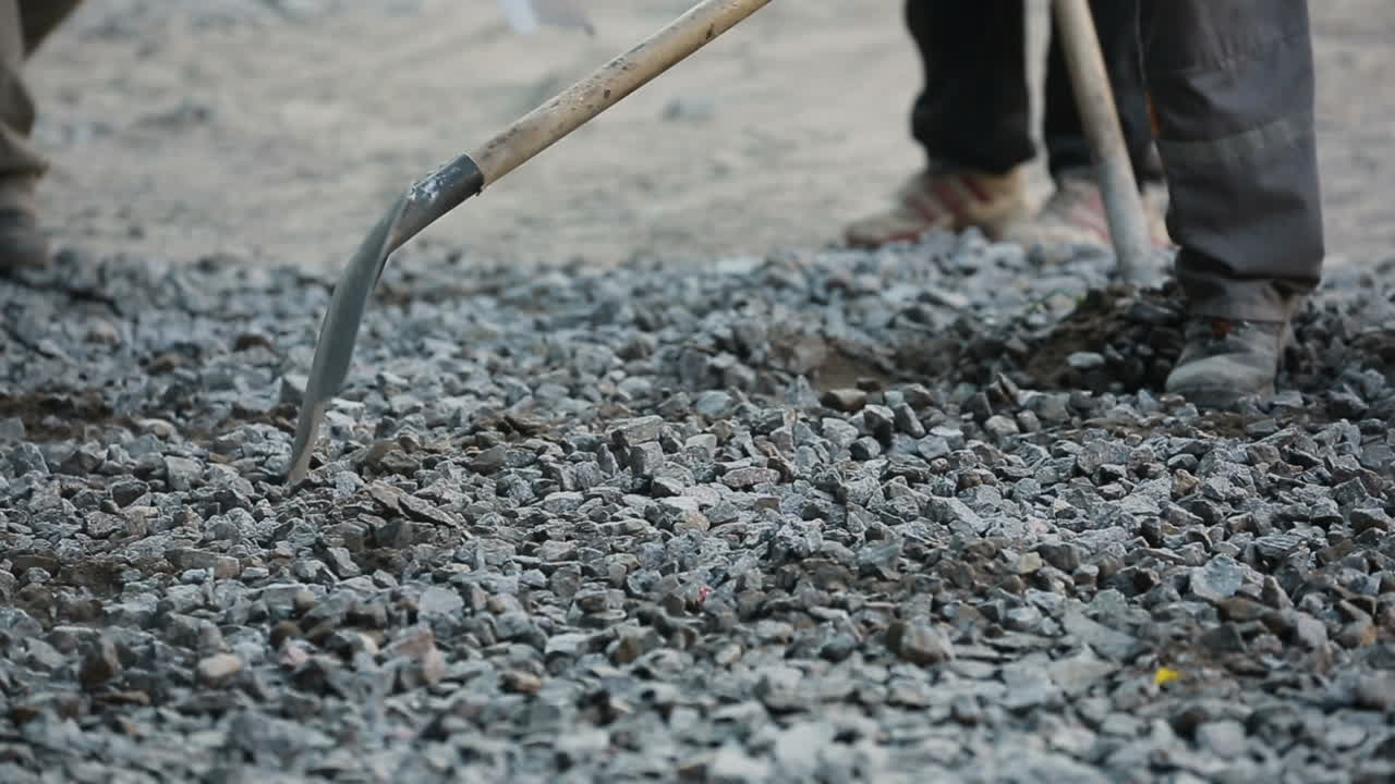Construction worker holding shovel with gravel working on road construction