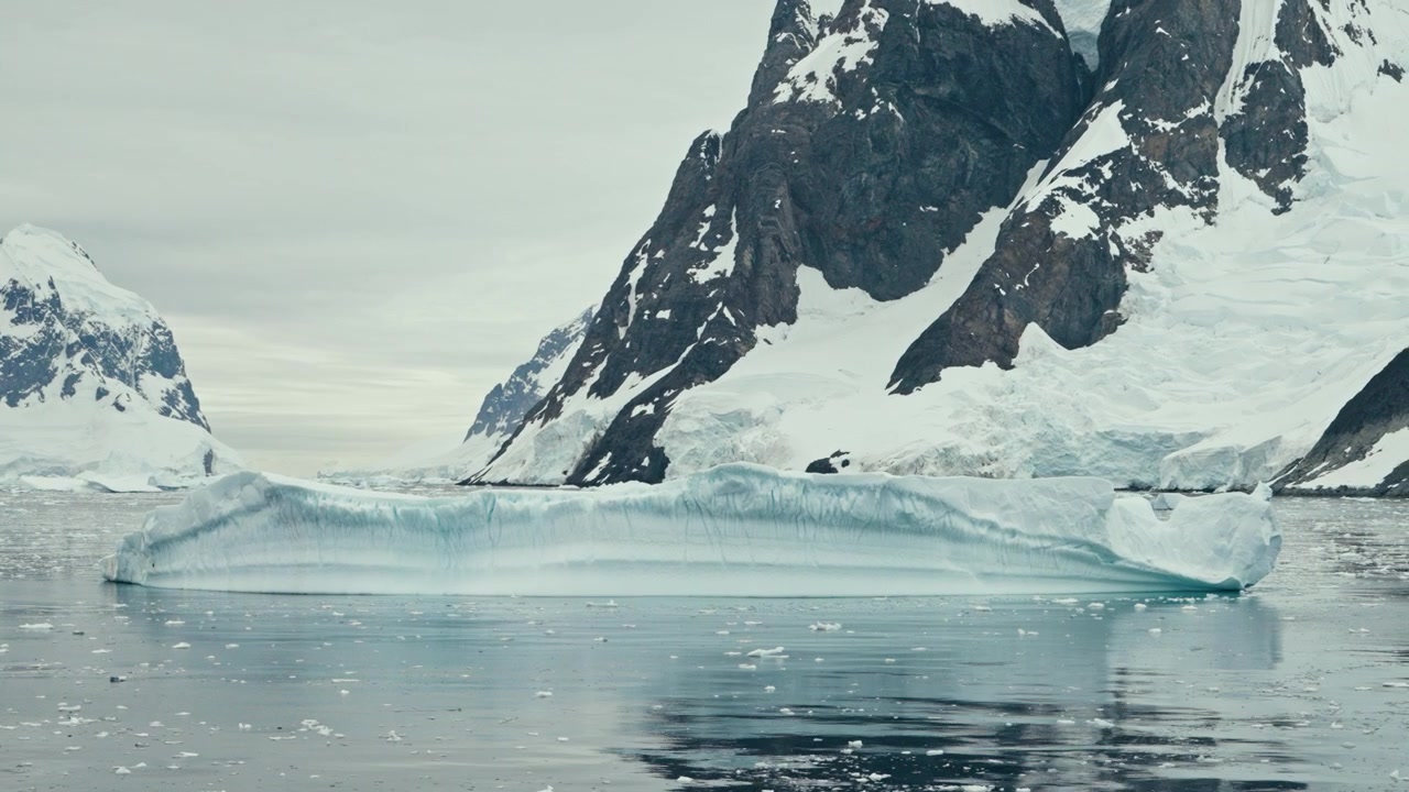 Iceberg tabular plano com reflexo perfeito na água flutuando no calmo Canal Lemaire, Antártica, ao lado de dramáticas falésias rochosas escuras