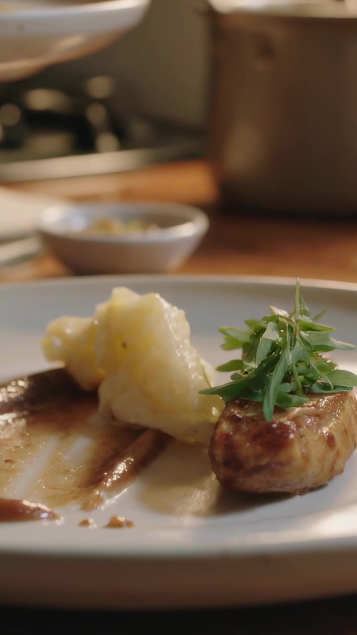 Vertical video: Hand reaching, chef placing microherbs on seared protein at pass, finishing plating