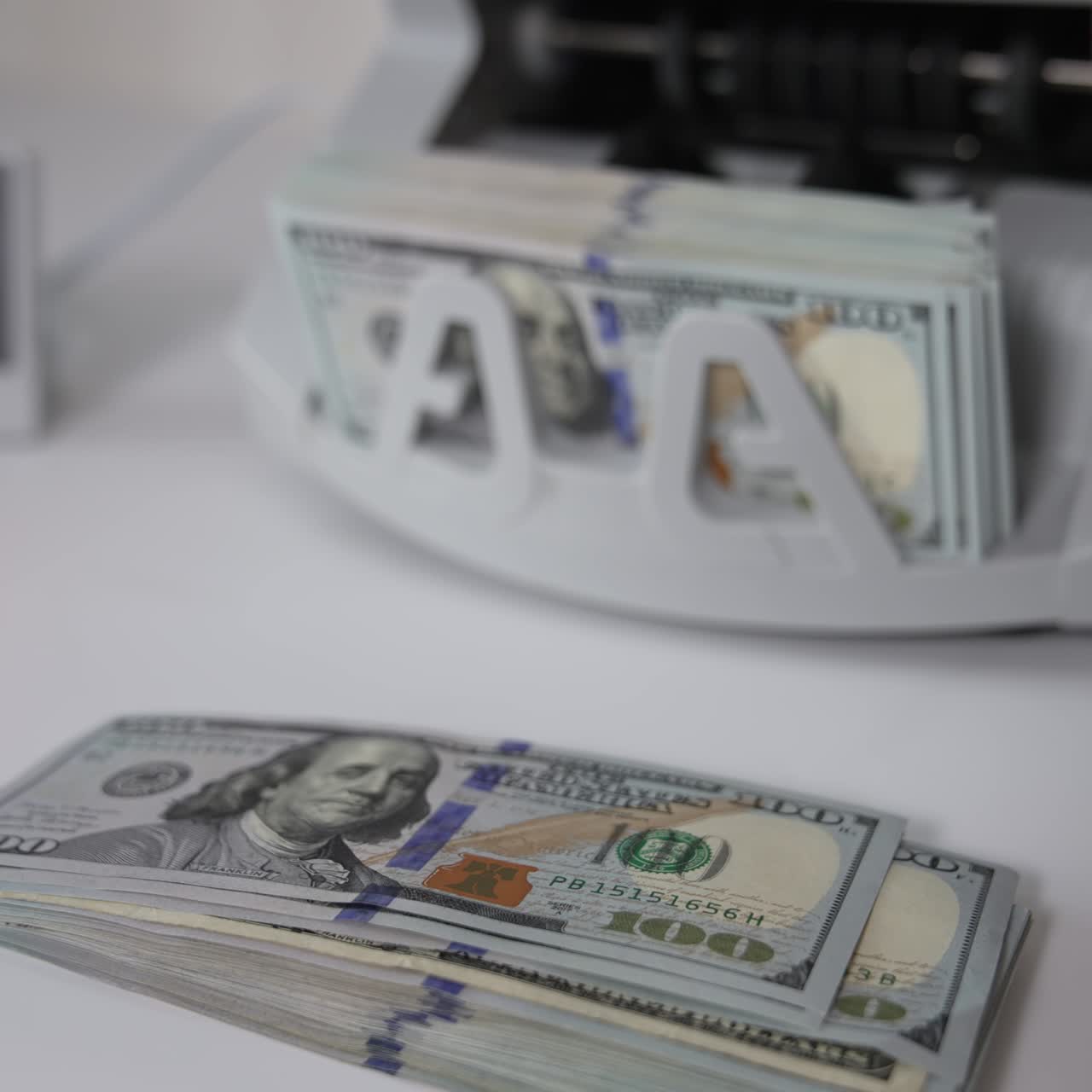 A wad of USD dollars is on the table. One hundred dollar bills are counted in the money machine. Blurred background