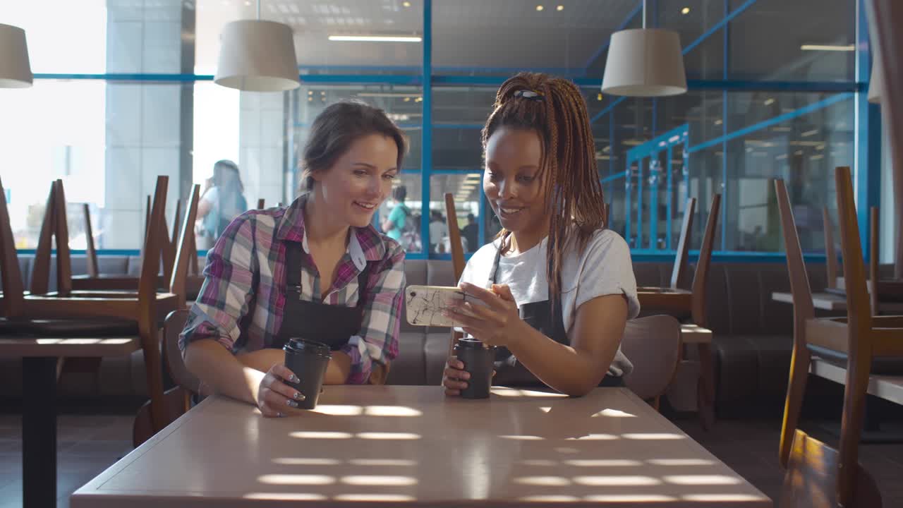 Diverse waitresses using smartphone in empty cafe before opening. Realtime