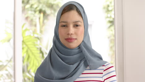 portrait of smiling biracial woman in hijab at home with copy space, slow motion