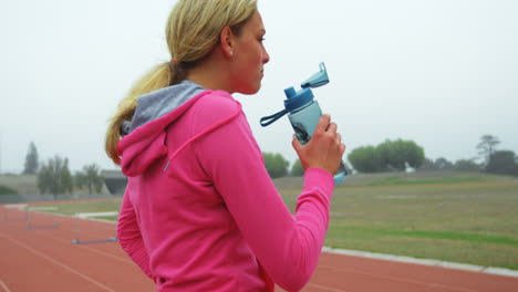 side view of caucasian female athlete drinking water on race track 4k