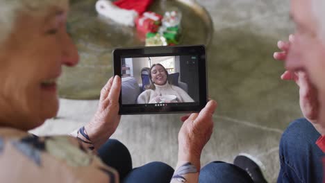 pareja caucásica mayor sonriendo y usando una tableta para una videollamada de navidad con una mujer en la pantalla