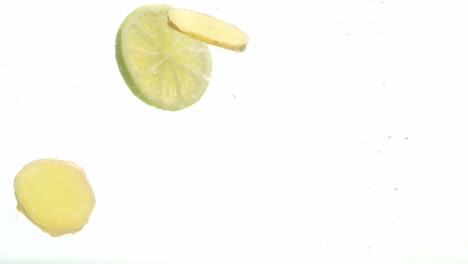 green lemon and ginger dropped into water, isolated white background