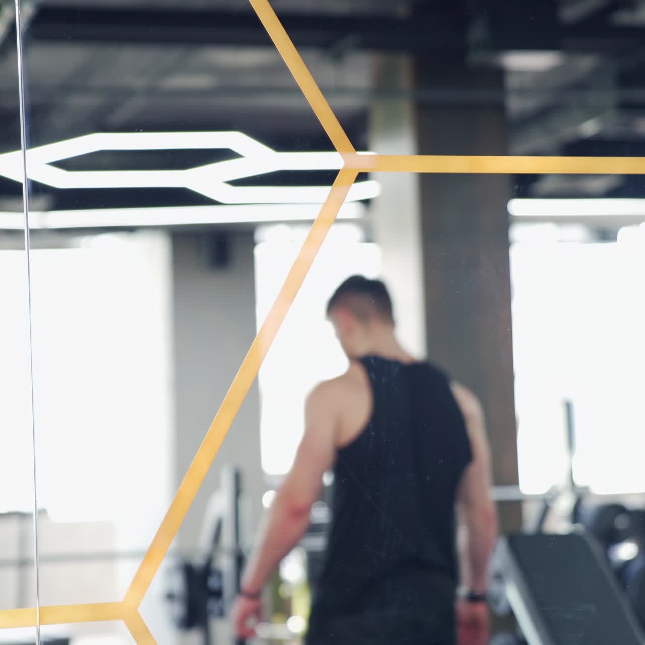 Sportsman in mirror reflection in fitness centre. Handsome athlete rests after hard training. Muscular bodybuilder indoors