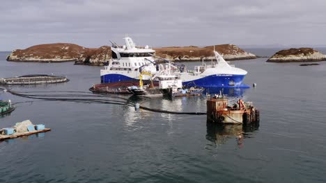 advancing drone shot of a fish farm cage being maintained by small ships