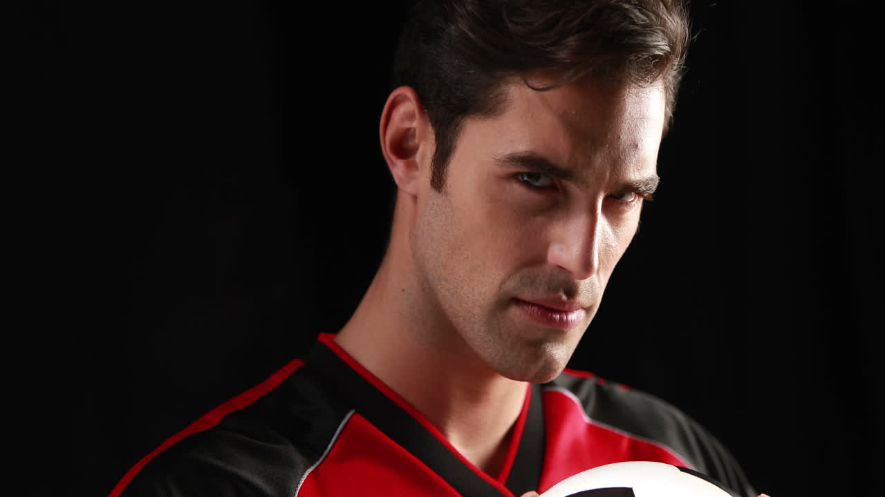 심각한 축구 선수가 공을 들고 카메라를 보고 있습니다.