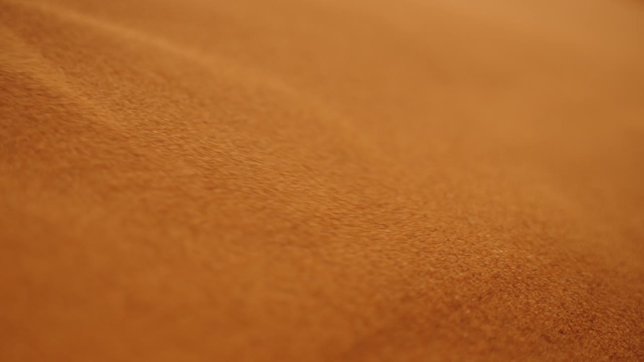 Golden Sahara desert sand sliding down a dune surface in soft warm evening light