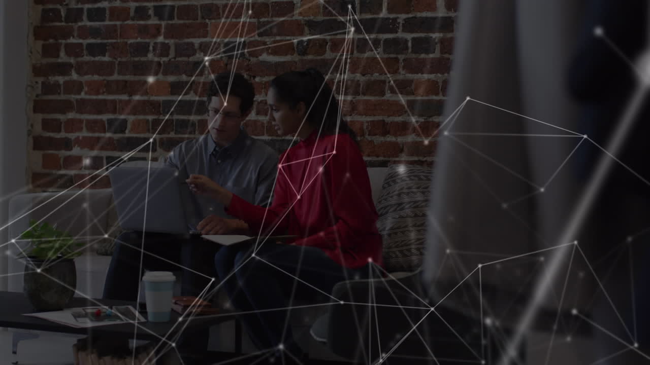Animation of network over male and female colleague using laptop on couch in office