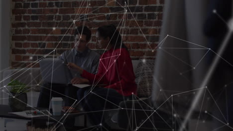 animation of network over male and female colleague using laptop on couch in office