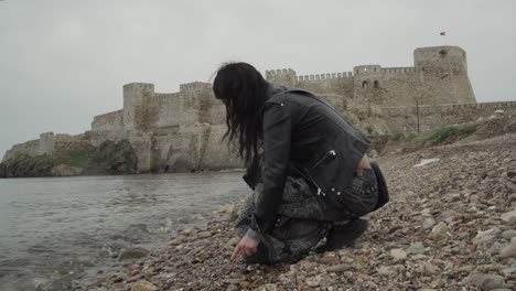 young and beautiful girl collecting stones on the seaside in front of a castle