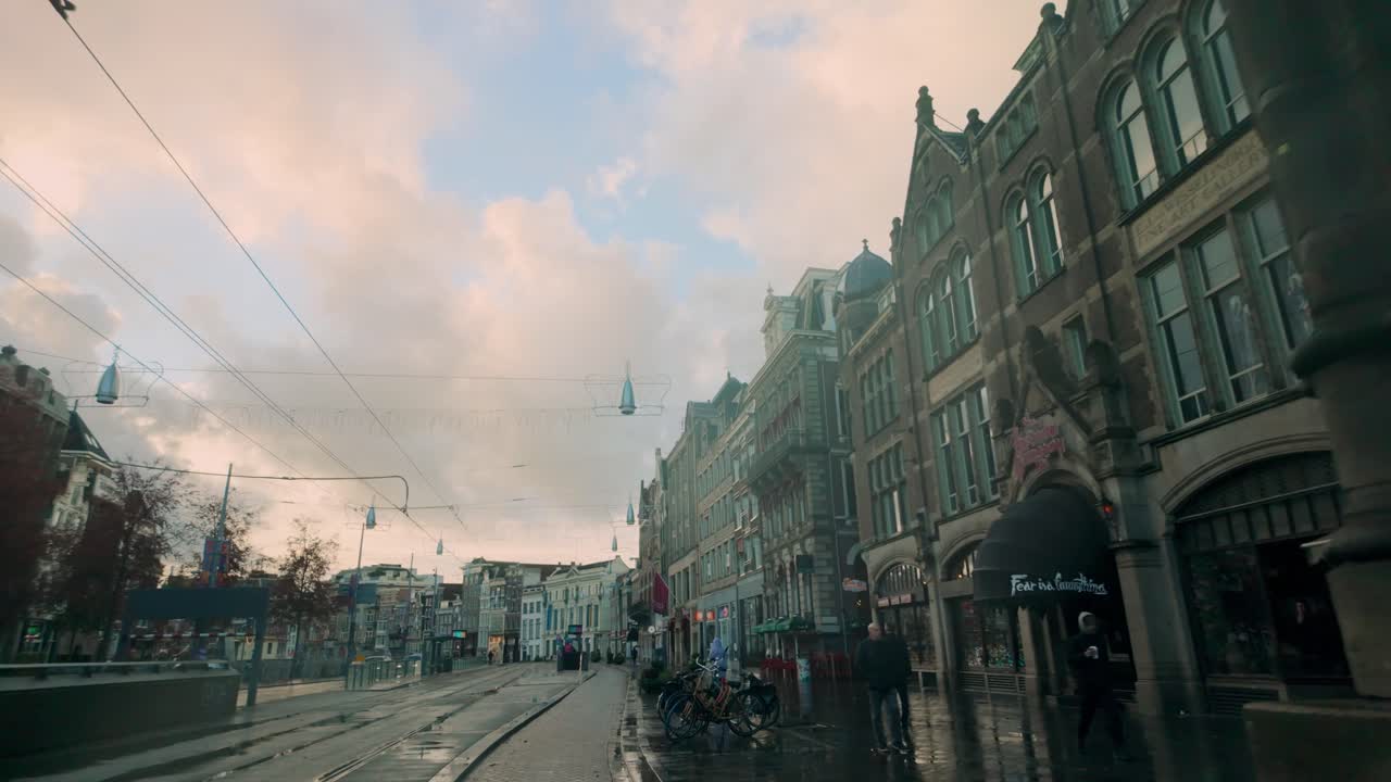 Rokin street in Amsterdam during the morning with tram tracks, historic architecture, and a prominent stone column. The calm atmosphere is enhanced by soft lighting and pastel skies