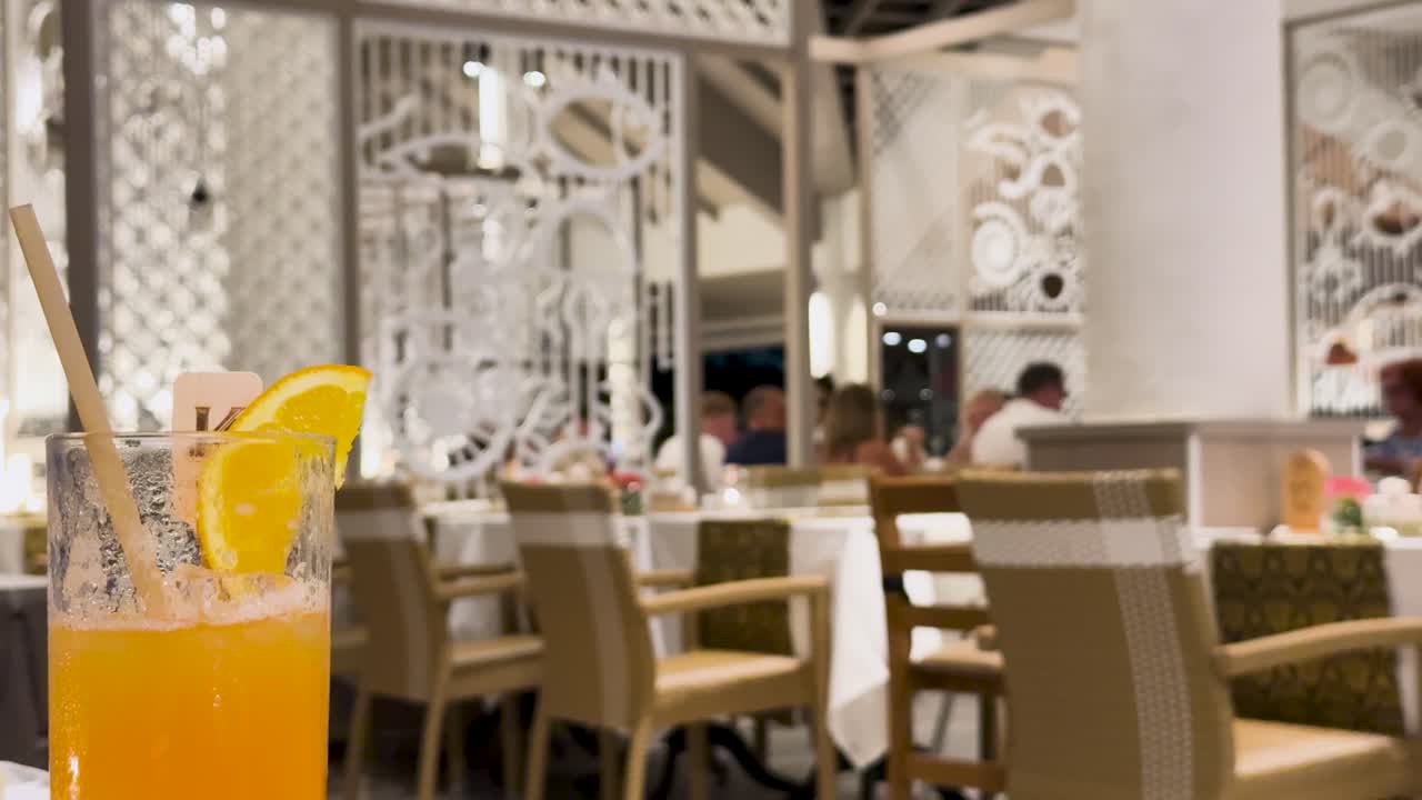 A vibrant orange cocktail with a straw and garnish sits on a table in a luxurious Phuket resort restaurant
