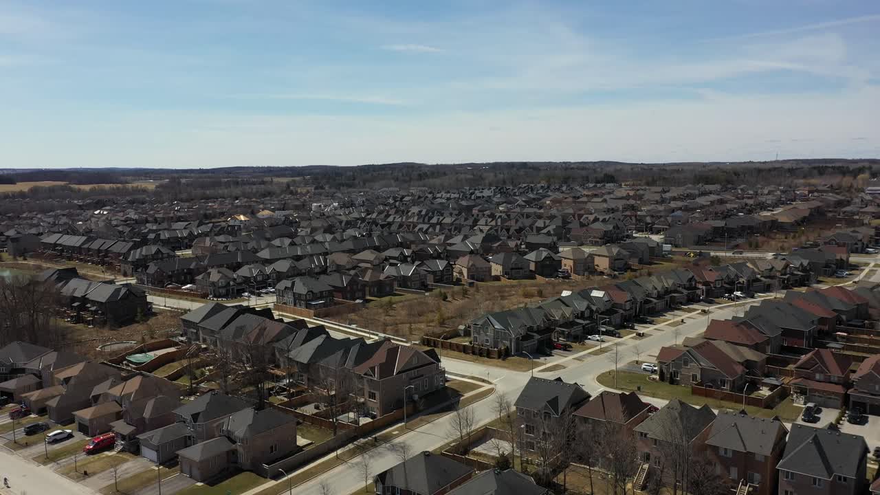 High altitude aerial footage revealing a vast frozen lake surrounded by a dense, snow covered forest and scattered houses, capturing the serene beauty of a crisp winter landscape