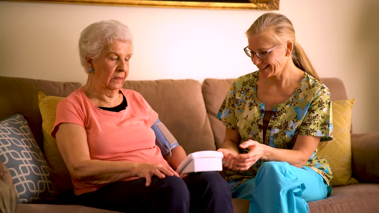 Home healthcare nurse and elderly woman taking blood pressure with a machine